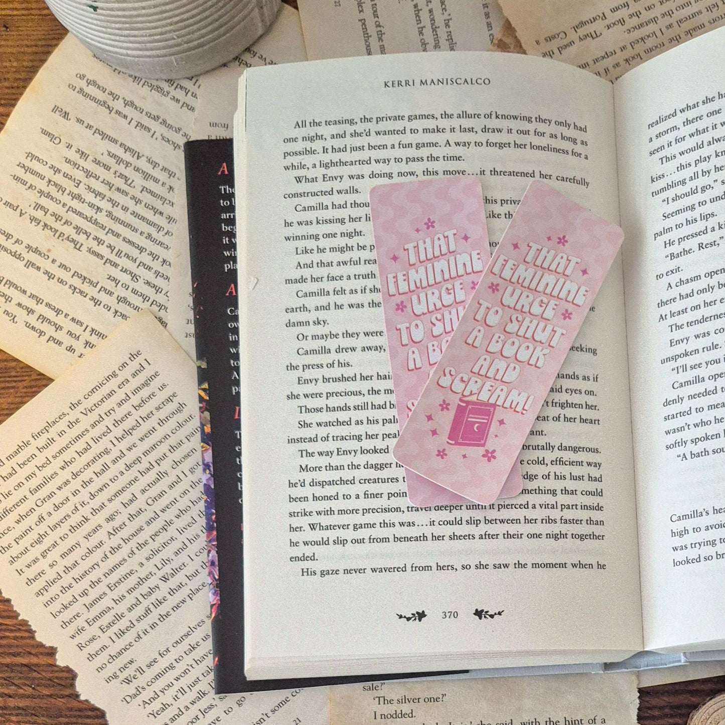That feminie urge to shut a book and scream! bookmark. Product flatlay. Product can be seen lying on an open book and surrounded by ripped pages on a table.