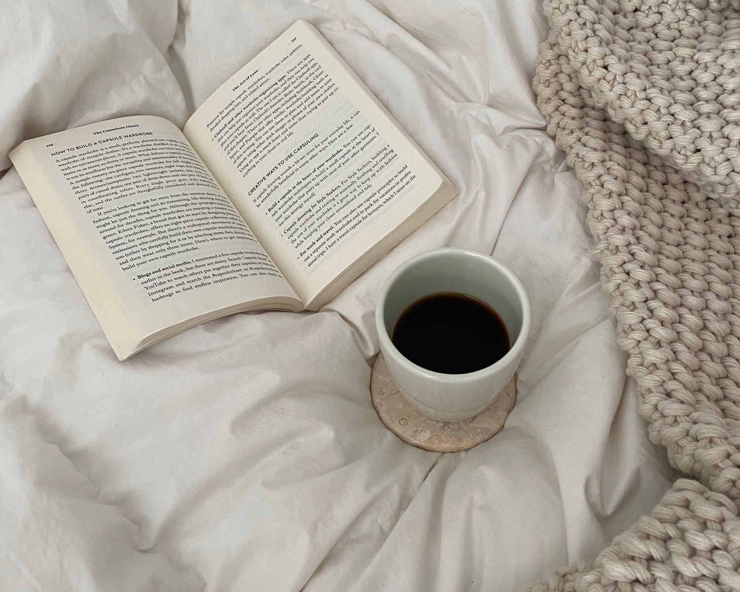 bookish flatlay ontop a white duvet cover with a cup of black coffee.