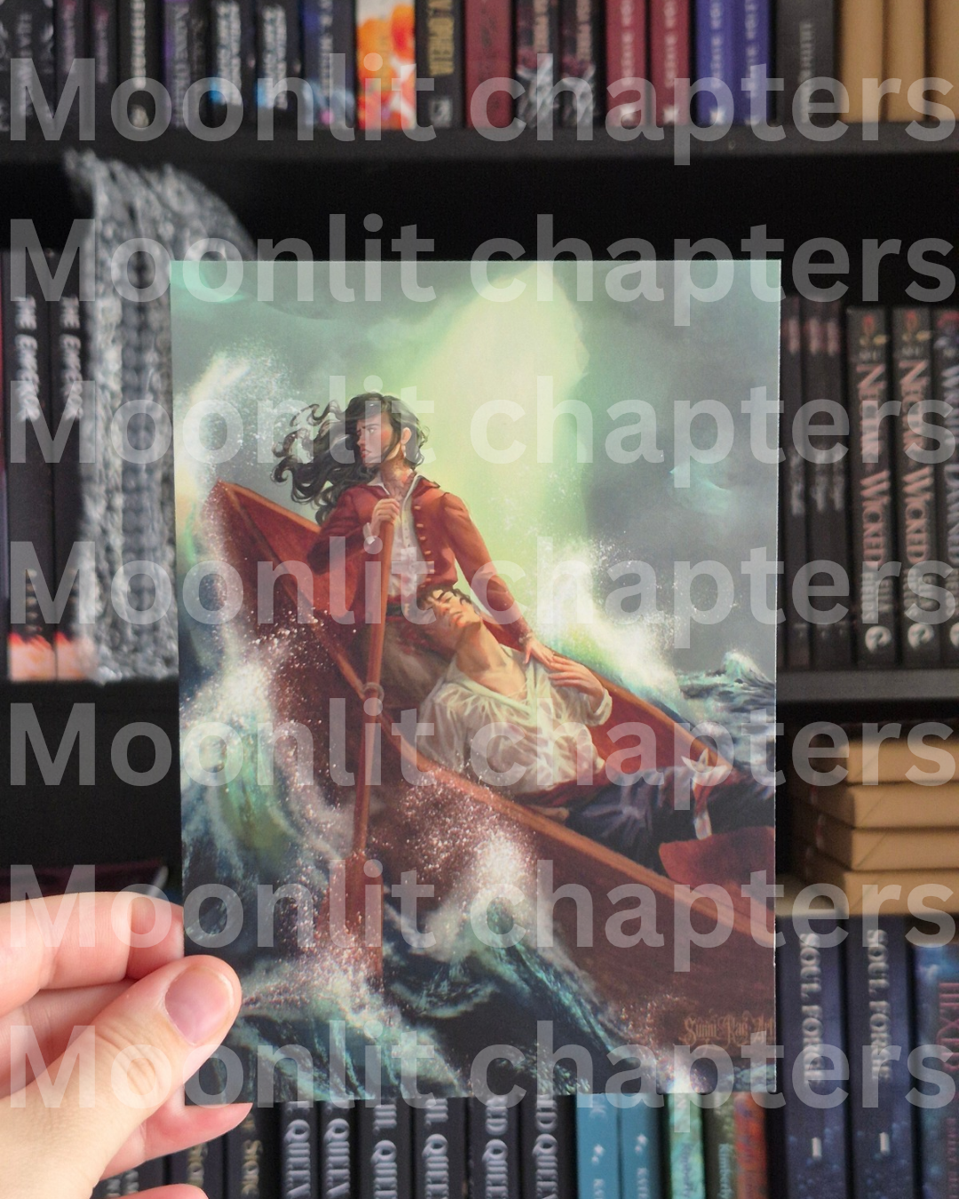 A hand holds a printed art card or postcard featuring an illustration of two people rowing in a boat through choppy waves, with a repeated watermark reading 'Moonlit chapters' across the photo. Bookshelves are visible in the background.