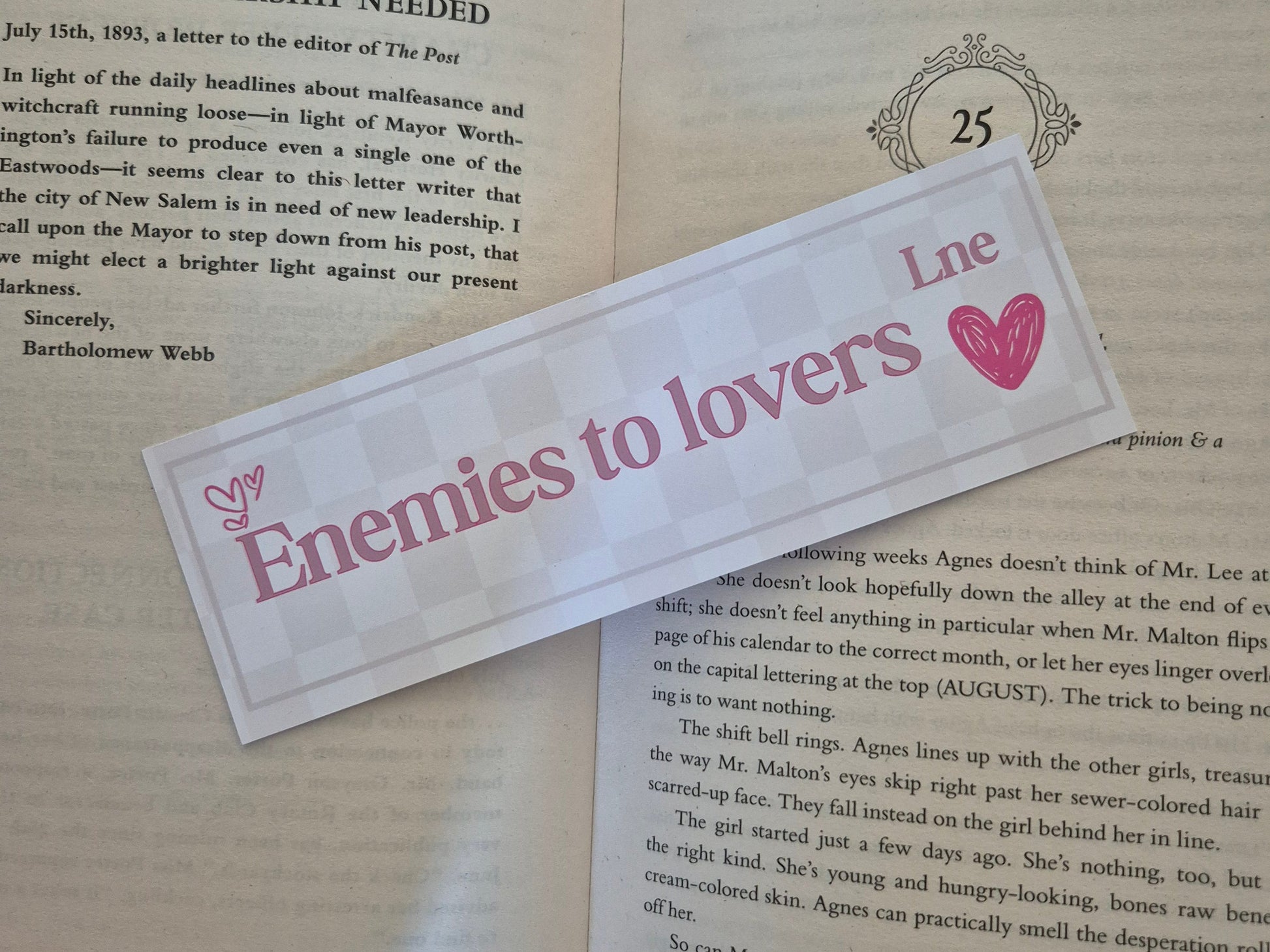 Bookmark with a chequered background with the words 'enemies to lovers Lne' on a open book