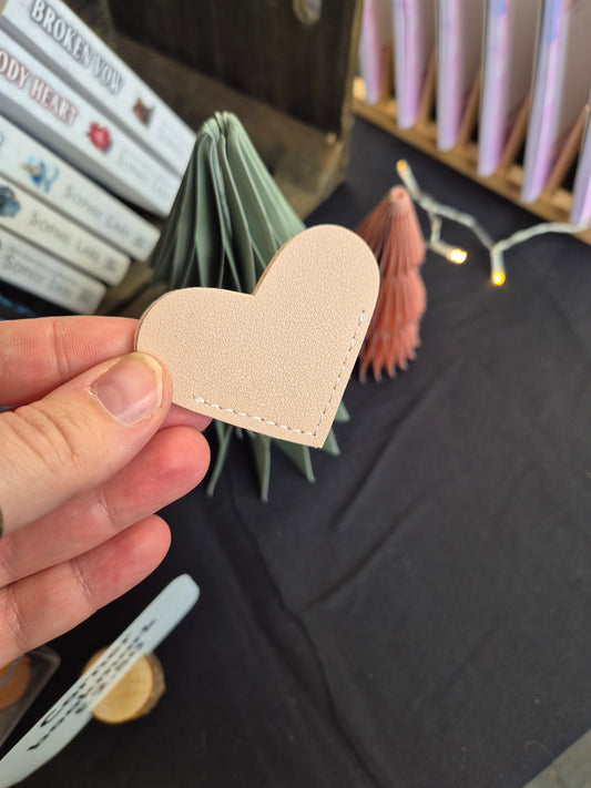 Heart-shaped beige corner bookmark held by a hand with a blurred background